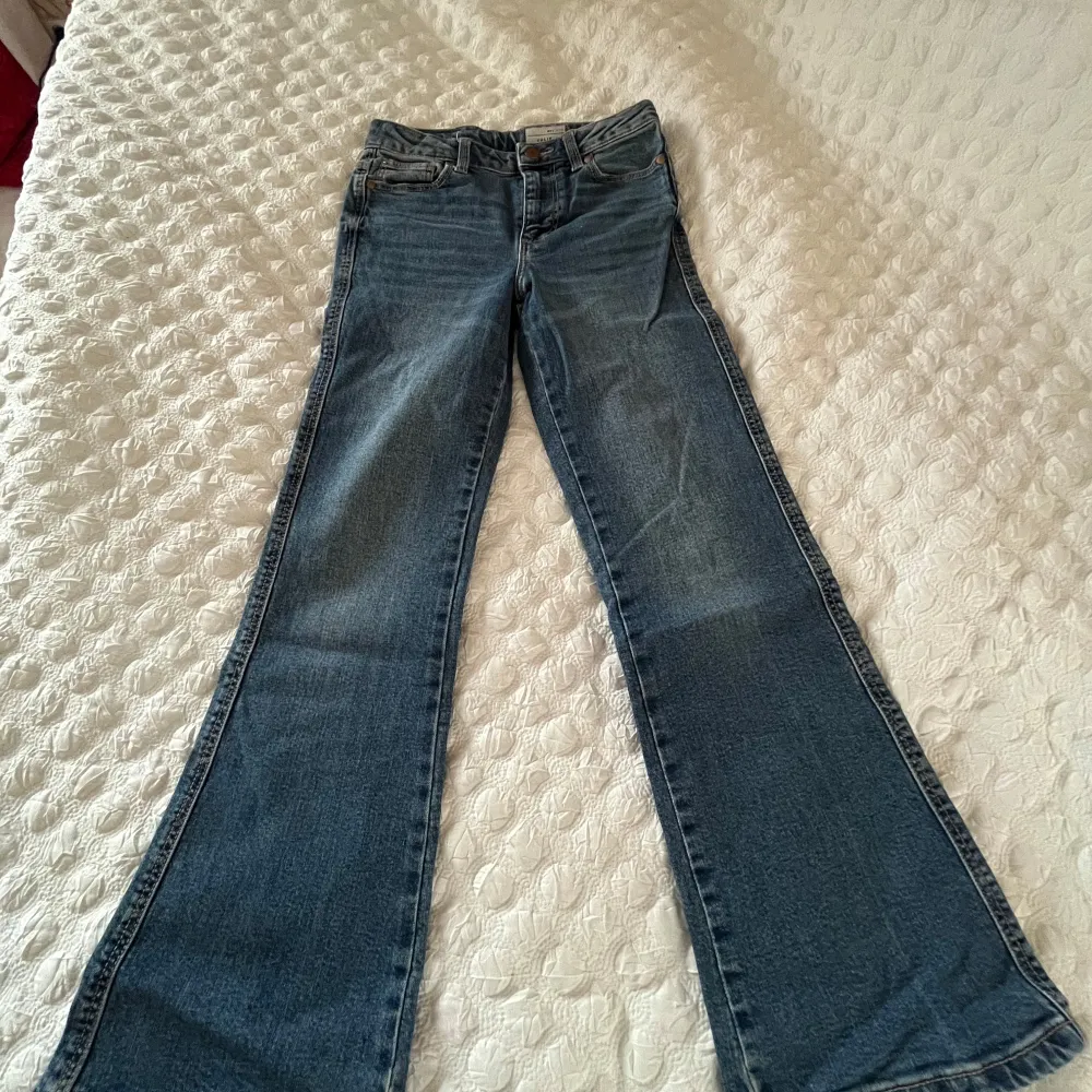 Snygga blå jeans från Cubus med hög midja och utsvängda ben. Perfekta för en trendig look. Dekorerade med en fjäril på baksidan för en extra touch av stil.. Farkut & Housut.