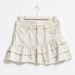 Beige volangkjol - Snygg beige kortkjol med volanger. Perfekt för en trendig look. Kjolen har en klassisk jeansstil med fickor. har inte anvont kjolen mer än kanske 3-4 gånger, jag säljer den för jag vet att den är populär och att jag inte använder den🥰