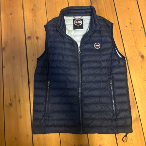 Mörkblå dunväst från Colmar - Säljer en snygg mörkblå dunväst från Colmar. Västen har dragkedja framtill och två praktiska fickor med dragkedjor. Perfekt för sommaren!. Märkeslogga på bröstet ger en stilren touch. Priset är ej hugget i sten 