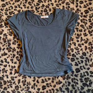 Mörkgrå kortärmad topp  - Säljer en stilren mörkgrå topp. Den har en rund halsringning och korta ärmar, perfekt för en avslappnad look. Materialet är mjukt och bekvämt, vilket gör den idealisk för vardagsbruk.