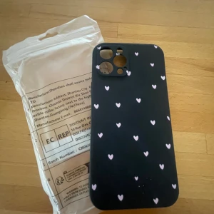 Svart mobilskal med hjärtan - Snyggt svart mobilskal dekorerat med små vita hjärtan. Perfekt för att ge din telefon ett stilrent och personligt utseende. Skalet är designat för att skydda baksidan och kanterna av din mobil.