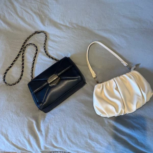 Svart axelväska med kedja och beige handväska - Två stiliga väskor till salu! En svart axelväska med kedjedetalj och metallspänne, perfekt för en elegant look. Den andra är en beige handväska med mjukt, veckat material. 
