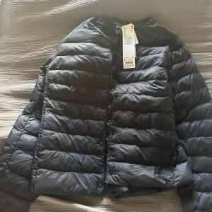 Svart jacka från Uniqlo - Säljer en svart jacka från Uniqlo. Jackan har knappar framtill och är designad för att vara lätt och hållbar. Perfekt för kyligare dagar. Storlek S, helt ny med prislapp kvar 