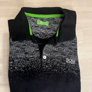 Hugo boss pikétröja Medium - Snygg svart pikétröja från Hugo Boss med ett unikt vitt mönster. Tröjan har en klassisk krage och knappar framtill. Storlek Medium