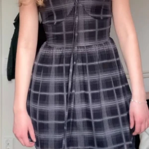 Svart och grå rutig klänning - Snygg svart och grå rutig klänning med knytning framtill. Perfekt för en stilren look. Klänningen har en normal passform och är ärmlös, vilket gör den idealisk för varmare dagar.