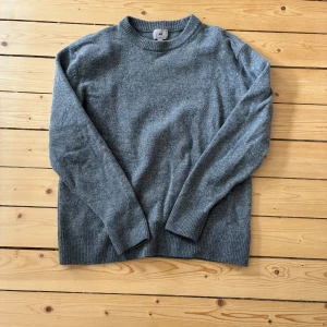 Grå stickad tröja från H&M - Säljer en stilren grå stickad tröja från H&M i regular fit. Tröjan har långa ärmar och ribbade muddar vid ärmslut och nederkant. Perfekt för kyligare dagar!