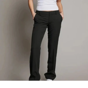 Svarta kostymbyxor - Snygga svarta kostymbyxor med normal passform som är lågmidjade bootcut. Byxorna har en klassisk design med dragkedja och knappar framtill. Perfekta för en stilren look. Modell ”Vera”