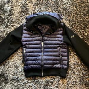 Levon jacka - Snygg pufferjacka i svart och blått med dragkedja och huva. Med avtagbar luva