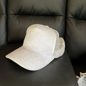 Vit keps med broderad logga - Snygg vit trucker keps med en broderad logga framtill. Kepsen är av märket maggiore. Kepsen har ett justerbart spänne baktill och mesh-paneler för extra ventilation. Perfekt för en avslappnad stil. Priset går att diskutera vid en snabb affär😁