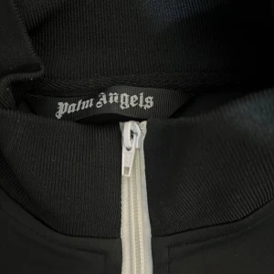 Palm Angels tröja  - Snygg svart träningsjacka från Palm Angels med vit dragkedja och logga på bröstet. Perfekt för en  avslappnad stil.