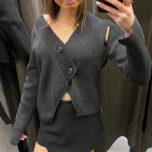 Mörkgrå Zara kofta - Jättesnygg kofta som är slutsåld ifrån Zara! Den är i storlek S och nästan oanvänd. Koftan är stickad och har två knappar, den har ett hål vid högra axeln som en cool detalj.