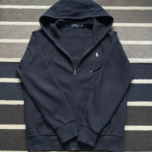 Svart hoodie från Ralph Lauren - Säljer en stilren svart hoodie från Ralph Lauren med dragkedja och det klassiska logotypbroderiet på bröstet. Perfekt för en avslappnad look. Hör av dig vid intresse!