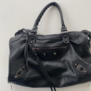 Svart handväska med dragkedja - Snygg svart handväska  med praktiska dragkedjor och stiliga detaljer. Väskan har robusta handtag och flera fack för enkel organisering. Perfekt för att bära med sig det viktigaste med stil. Det förekommer defekter! (Se bild) och medföljer ett oanvänd axelband. Skriv för att buda eller fler bilder. PS IDAG ÄR DET FRIFRAKT PÅ ALLA VÄSKOR