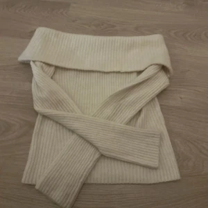 Beige ribbad offshoulder tröja från H&M - Säljer en stilren beige ribbad offshoulder tröja från H&M. Tröjan har långa ärmar och en bred krage som ger en elegant look. Perfekt för att hålla sig varm och snygg under kyligare dagar. Passar bra till både jeans och kjol.