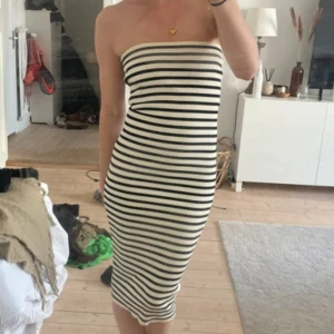 Klänning  - Snygg axelbandslös klänning med svartvita ränder. Den har en tight passform och är ribbad, vilket ger en stilren look. Perfekt för sommarens varma dagar.