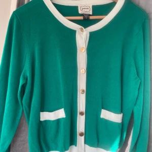 Kofta - Säljer en snygg grön kofta med vita detaljer och knappar framtill. Koftan har långa ärmar och två praktiska fickor. Perfekt för en stilren look!