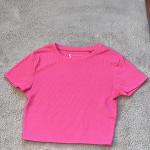 Rosa ribbad topp från FSBN Sister - Snygg rosa ribbad topp från FSBN Sister i storlek S. Denna kortärmade topp har en croppad passform och är perfekt för en trendig look. Tillverkad i ett mjukt och bekvämt material.