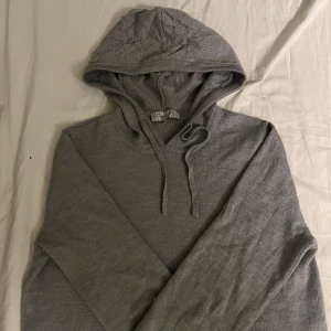 Grå hoodie från Ahlquist Clothing - Säljer en stilren grå hoodie i merino ull från Ahlquist Clothing. Tröjan har en klassisk design med huva och dragsko, perfekt för en avslappnad look. Passar bra till både jeans och joggers. Perfekt för kyliga dagar!