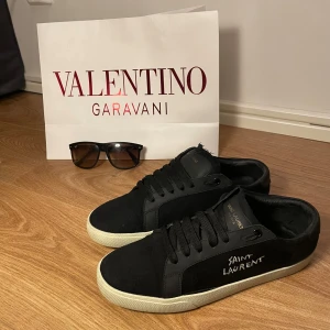 Svarta sneakers från Saint Laurent - Snygga svarta sneakers från Saint Laurent med vit sula och diskret logga på sidan. Skorna har klassisk snörning och en stilren design som passar perfekt för en trendig look. Passar 42-43. Skriv för mer info🤩💫 extremt bra skick
