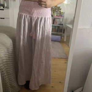 Rosa långkjol från Gina Tricot - Säljer en söt rosa långkjol från Gina Tricot. Kjolen har en smockad midja och dekorativa tofsar framtill. Perfekt för en avslappnad och stilren look. 🌸