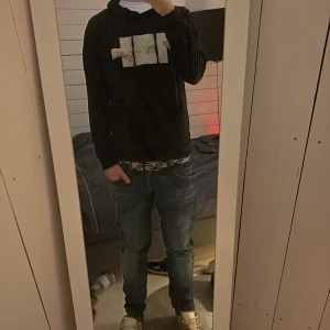 Svart hoodie med konsttryck - Säljer en svart hoodie med ett konstnärligt tryck av två händer på framsidan. Hoodien har en klassisk passform med långa ärmar och en stor ficka framtill. Perfekt för en avslappnad stil. Litet hål i armhålan