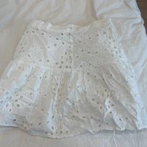 Vit broderad kortkjol från Amisu - Superfin vit kortkjol från Amisu med broderade hål och volangdetaljer. Kjolen har resår i midjan för extra komfort och är perfekt för varma dagar. Snygg och luftig modell som ger en fräsch look.