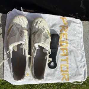 Adidas Predator Elite vita/guld - Säljer ett par Adidas Predator elite i vitt och guld – ikoniska skor för den som vill dominera på planen! Använda men i bra skick. Skorna levereras med originalpåse och skohorn från adidas. Perfekta för dig som vill ha känsla och kraft i varje passning och skott!                                           Nypris: ca 3200