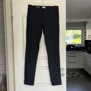 Grå slim fit kostymbyxor från Jack & Jones - Snygga grå kostymbyxor från Jack & Jones i slim/ Marco fit-modell. Byxorna har diskret mönster, bälteshällor, knapp och dragkedja i gylfen samt bi-stretch för extra komfort. Perfekta för en stilren look.