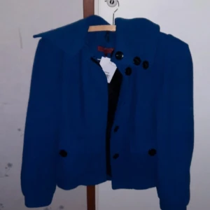 Blå kappa från John B Richmond - John Richmondjacka köpt på Zalandos second handsida, men aldrig använd av mig. En knapp lossnade dock när jag provade jackan, för att jackan är för liten, men knappen finns kvar och medföljer. Skicket är utmärkt och det finns inga andra tecken på användning. Det står storlek 36, men jag skulle säga att den sitter som en 34. Jag brukar ha 36 och den är för liten för mig.