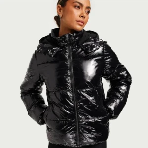 Nellys glansiga pufferjacka - svart glansig pufferjacka med huva och dragkedja framtill. Jackan har lång ärm och en modern, lite oversized passform. Perfekt för kyliga dagar när du vill hålla värmen och ändå se snygg ut. Säljer för att ja inte använder längre. Den den har haft ett litet hål i ryggen men har fixat det så det knappt syns❤️