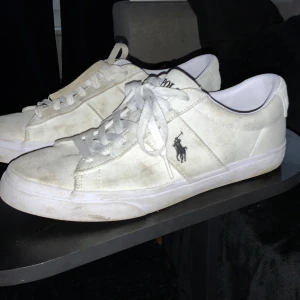 Vita sneakers från Polo Ralph Lauren - Säljer ett par klassiska vita sneakers från Polo Ralph Lauren med snörning och rund tå. Skorna har Polo-loggan broderad på sidan och märket tryckt på hälen. Perfekta till en avslappnad stil.