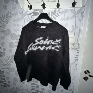 Saint Laurent Sweatshirt  - Säljer en svart stickad tröja från Saint Laurent med vit logotyp framtill. Tröjan har rund halsringning och långa ärmar. Perfekt för dig som vill ha en stilren och lyxig look. OBS! PRISET KAN DISKUTERAS VID EN SNABB AFFÄR!