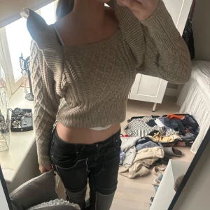 Beige croppad stickad tröja - Säljer en beige croppad stickad tröja med kabelstickat mönster och långa ärmar. Tröjan har bredare halsringning och ribbade muddar. Perfekt för dig som gillar en trendig och mysig stil.
