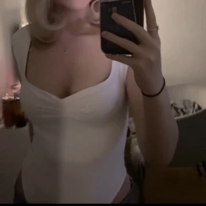 Vit croppad body med breda axelband - Säljer en vit croppad body med breda axelband och lätt rynk vid bysten. Bodyn har en djup, rundad urringning och är figurnära i modellen. Perfekt för en stilren och enkel look. Storlek M men skulle säga att den sitter som en S.