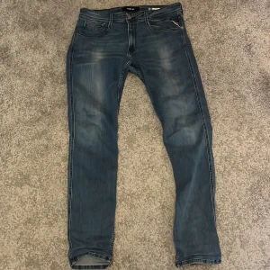 Replay Anbass jeans - Säljer ett par Replay Anbass jeans i klassisk blå denim. Byxorna har fem fickor, raka ben och snygga slitningar framtill. Märkeslapp bak i midjan och diskreta detaljer på bakfickorna. Perfekta för dig som gillar stilrena jeans med modern passform.