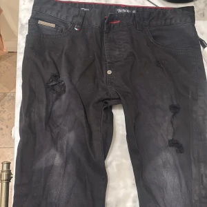 Philipp Plein svarta jeans, illegal fight club kollektionen - Svarta jeansbyxor från Philipp Plein med super straight cut. Tog nyss ut de från garderoben så de är lite katthår på dem, det tas naturligtvis bort vid köp. Byxorna kommer från illegal fight club-kollektionen och  har slitna detaljer på framsidan, klassiska fem fickor och en knapp med dödskallemotiv. Röd kontrastsöm i midjan och diskret logga på bakfickan. Köptes av min far 2021 från Mintuu men då de ej passade mig eller honom så fick de ligga. Digitalt kvitto finns, skriv vid frågor! 💸
