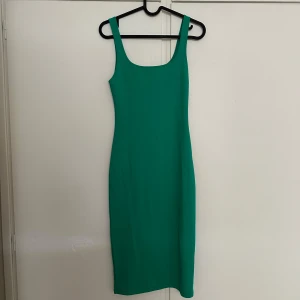 Grön tight ärmlös klänning - Säljer en smaragdgrön tight klänning med djup rundad ringning och breda axelband. Klänningen är ärmlös och har en slits baktill för extra rörelsefrihet. Perfekt för dig som gillar en enkel men stilren look.