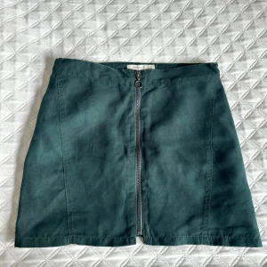 Mörkgrön kjol med dragkedja från Name It - Snygg mörkgrön kortkjol från Name It med en synlig dragkedja framtill. Kjolen har en enkel, rak passform och är perfekt för dig som gillar stilrena plagg med en twist.