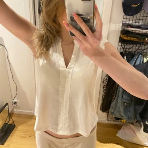Vit ärmlös blus med spetsdetaljer - Säljer en stilren vit blus med v-ringning och spetsdetaljer på axlarna. Blusen är ärmlös och har en rak passform, perfekt till sommaren. Materialet känns lätt och luftigt. Princip aldrig använt så i bra skick☺️