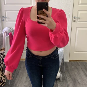 Rosa croppad topp med puffärmar från SHEIN - Säljer en snygg rosa croppad topp från SHEIN med långa puffärmar och fyrkantig ringning. Toppen har en figurnära passform och är perfekt för att lyfta vilken outfit som helst. Materialet är mjukt och stretchigt.