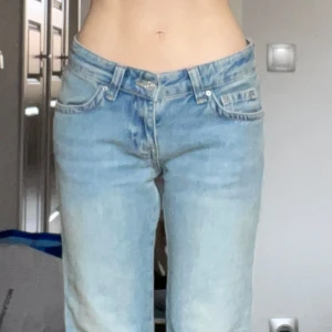 Ljusblå bootcut jeans med låg midja - Säljer ett par ljusblå jeans med bootcut passform och låg midja. Jeansen har klassiska fem fickor, bälteshällor och stängs med dragkedja och knapp. Perfekta för dig som gillar en avslappnad och trendig look.