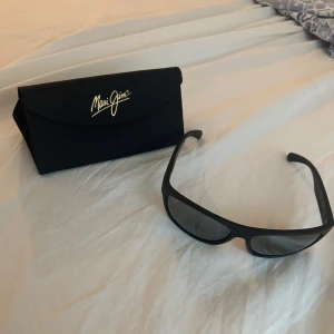 Svarta solglasögon från Maui Jim Tumbleland - Snygga svarta solglasögon från Maui Jim, modell Tumbleland. De har en sportig design med breda skalmar och mörka glas. Perfekta för soliga dagar och tillverkade i Italien. Kommer med originalfodral. Har använd ett par gånger men gillade inte den..