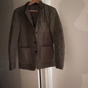 Quiltad kavajjacka från Tiger of Sweden - Säljer en stilren quiltad kavajjacka i mörkgrön från Tiger of Sweden. Jackan har tre knappar framtill, stora fickor och klassisk krage. Perfekt för dig som vill ha en dressad men ändå avslappnad look. 