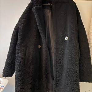 Svart teddyjacka från PLT - Mysig svart teddyjacka från prettylittlething med lång ärm och rak passform. Jackan har en enkel knäppning framtill och är fodrad på insidan. Perfekt för kyliga dagar och ger en trendig look.