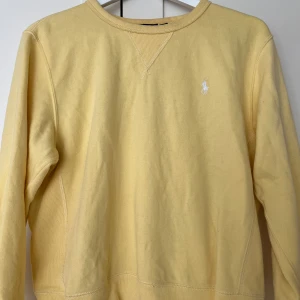Gul sweatshirt från Polo Ralph Lauren - Säljer en ljusgul sweatshirt från Polo Ralph Lauren med klassisk rund halsringning och broderad logga på bröstet.