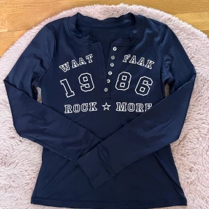 Mörk blå långärmad topp med tryck och knappar - Cool mörk blå långärmad topp från Temu med tryck 'WAAT FAAK 1986 ROCK MORE' framtill. Tröjan har sex knappar vid halsen och är gjord i ett stretchigt syntetmaterial. Perfekt för en avslappnad och trendig look.