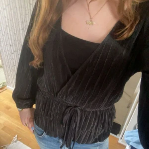 Svart blus - Säljer en svart blus i mjukt material med knyt i midjan. Jackan har långa ärmar och en elegant v-ringning. Perfekt för dig som vill ha en stilren och trendig look.