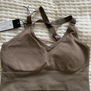 Ribbad sport-bh med korsade axelband - Säljer två ribbade sport-bh:ar från lager 157 i färgerna beige och svart. Båda har korsade axelband i ryggen och bred resår. Prislapparna är kvar och vadderingen går att ta ut. Säljer båda för 120kr 