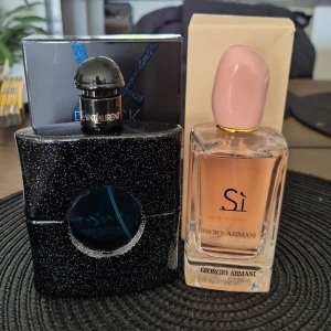 Yves Saint Laurent Black Opium & Giorgio Armani Sì parfym - Två parfymer: Black Opium från Yves Saint Laurent i en svart, glittrig flaska med rund detalj och Black Opium-logga, samt Sì från Giorgio Armani i en elegant, rektangulär glasflaska med ljusrosa lock och beige kartong. Endast testade, båda i 100 ml.