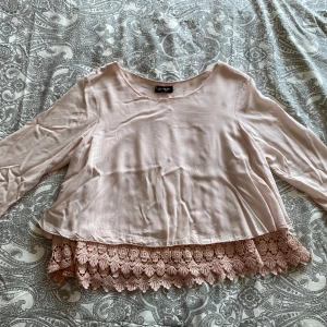 Ljusrosa blus med spetsdetalj - Säljer en ljusrosa blus med trekvartsärm och vacker spetskant nertill. Blusen är tillverkad i 100% viskos och har en lös passform. 